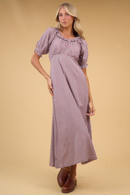 Young woman wearing a brown gingha midi dress with an empire waist, gathered bodice, short sleeves and a ruffled scoop neckline.