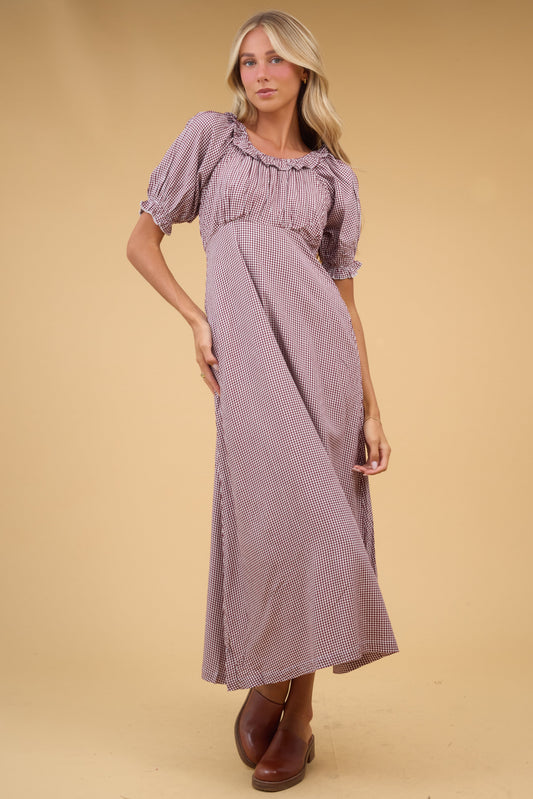Young woman wearing a brown gingha midi dress with an empire waist, gathered bodice, short sleeves and a ruffled scoop neckline.