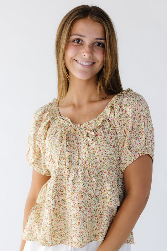 Young woman wearing a modest yellow floral print blouse with a scoop neckline, short puff sleeves, and empire waist and a double ruffle bottom.