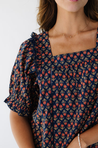 Close view of a young woman wearing a navy floral top with a square neckline and short puff sleeves with ruffle edge.