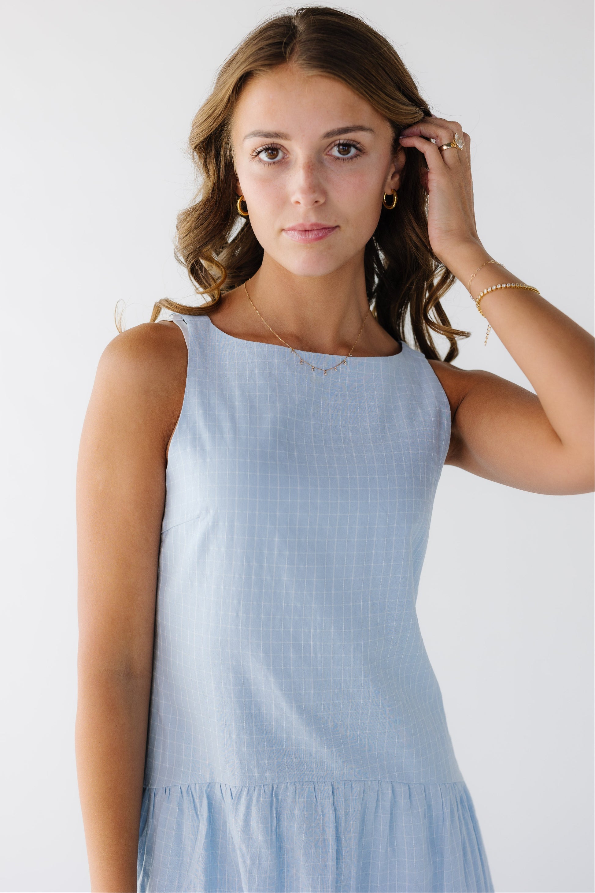 Closer view of a young woman wearing a light blue plaid sleeveless dress with a drop waist.