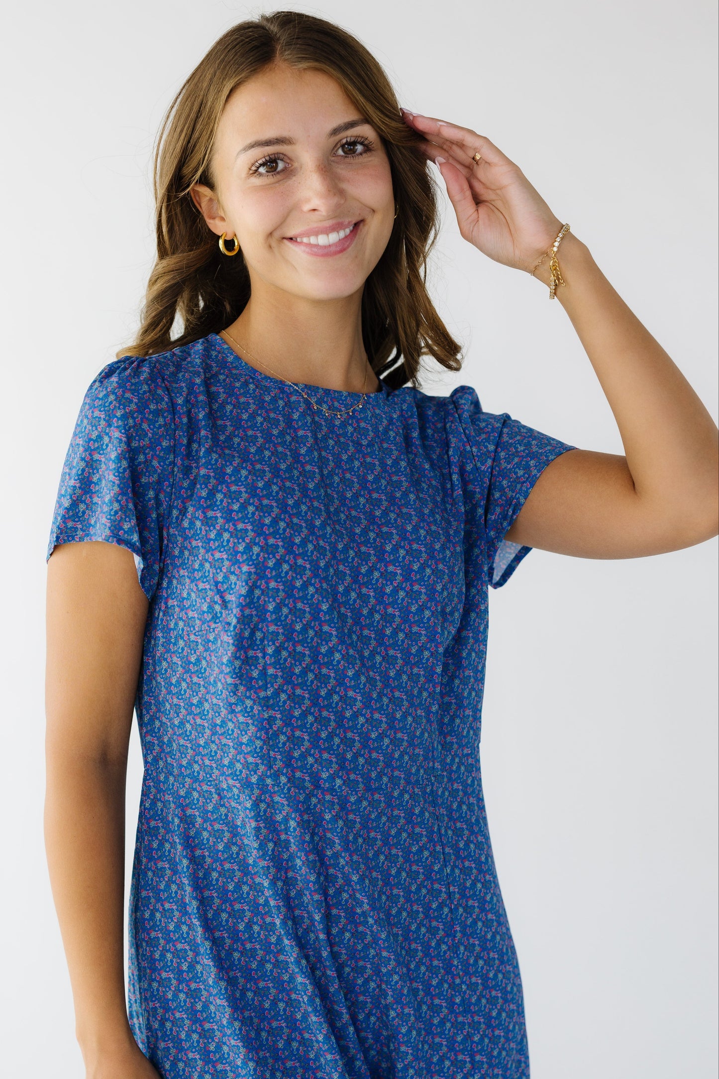 Close view of a young woman wearing a blue floral print sheath dress with a round neckline and short sleeves.