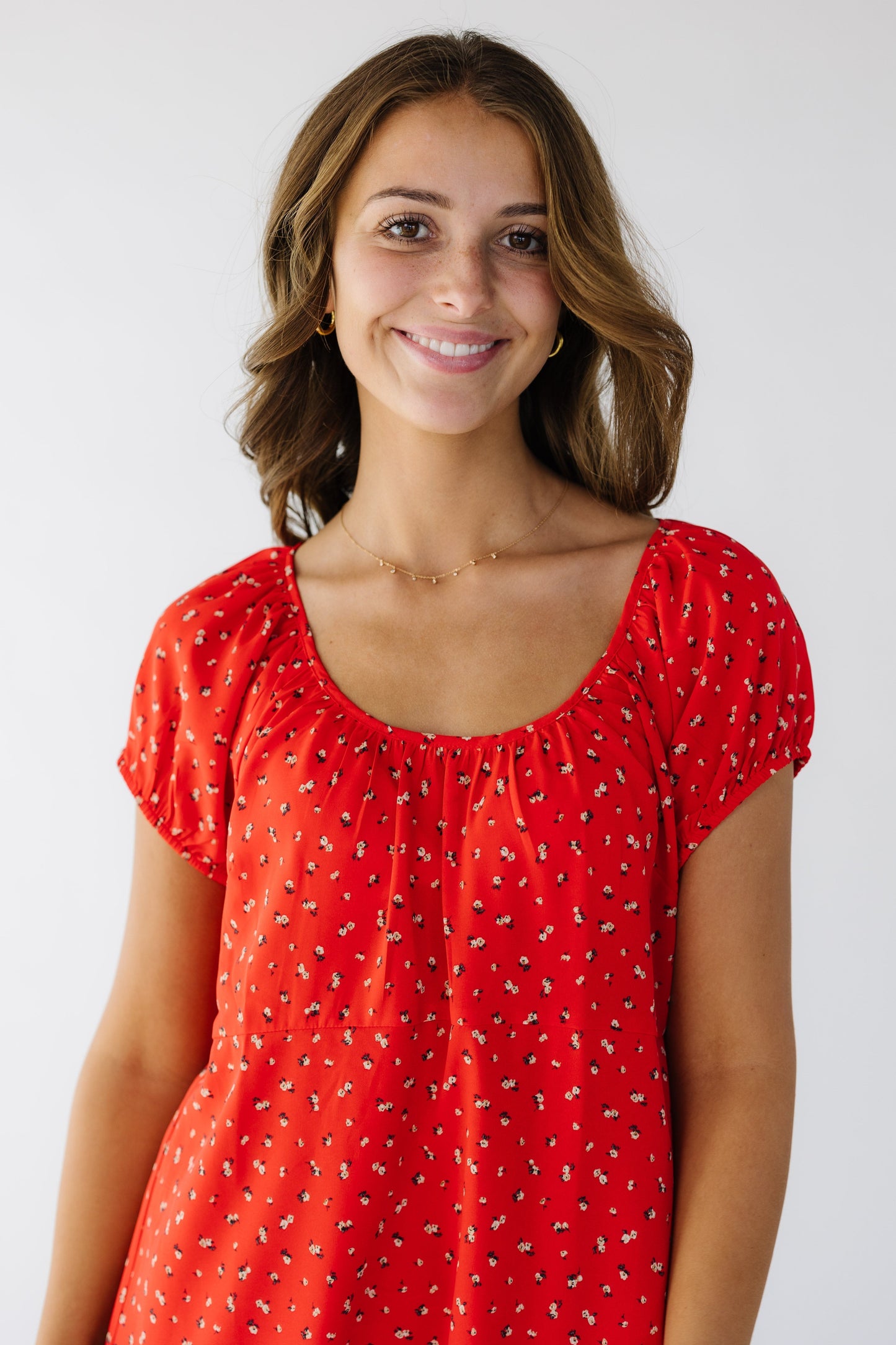 Close-up view of a young woman wearing a red floral swing dress with a scoop neckline.