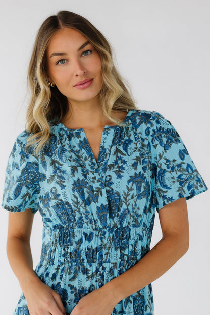 Young woman wearing a blue floral & paisley dress with a V-neckline, short sleeves and a wide elastic waist.
