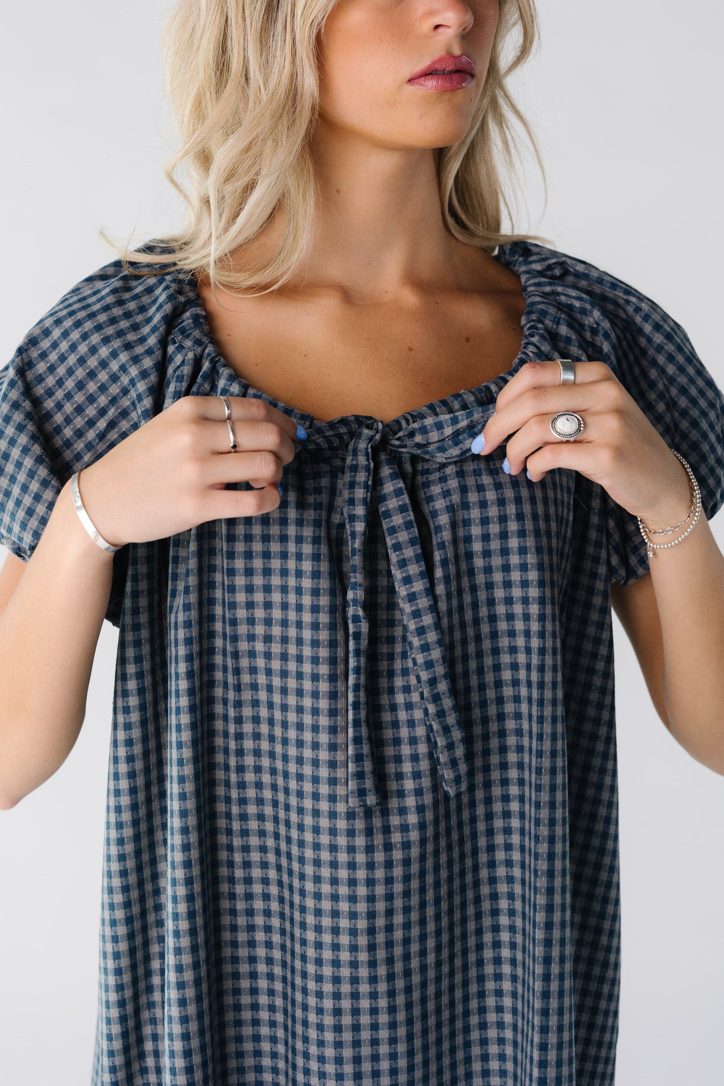Close view of a woman wearing a blue gingham dress with scoop drawstring neckline