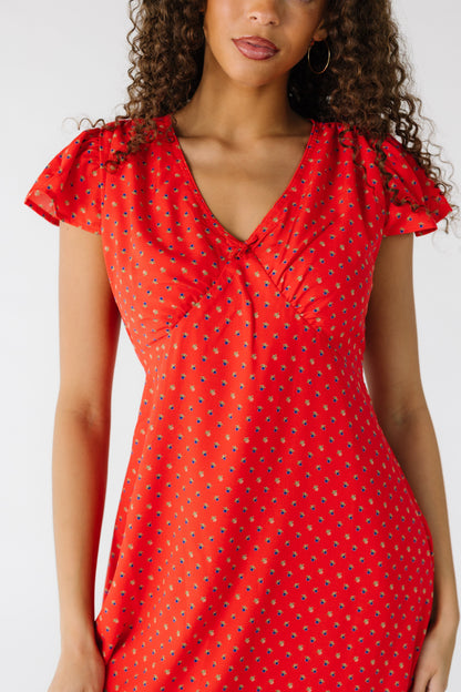 Close view of a teenage girl wearing a red floral print dress with a pointed empire waist and a V-neckline.