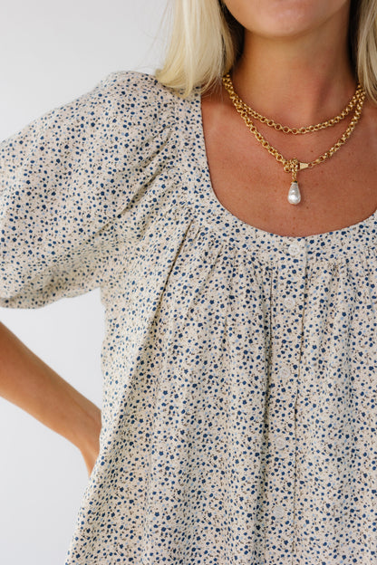 Close view of a woman wearing a cream & blue floral print dress with large puff sleeves and a scoop neckline.