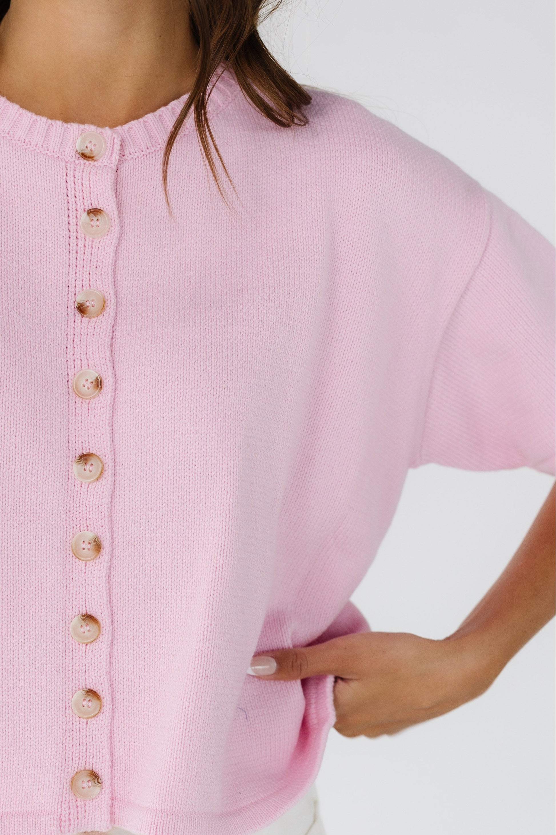Close view of a woman wearing a pink button down the cardigan with short sleeves and a crew neckline.