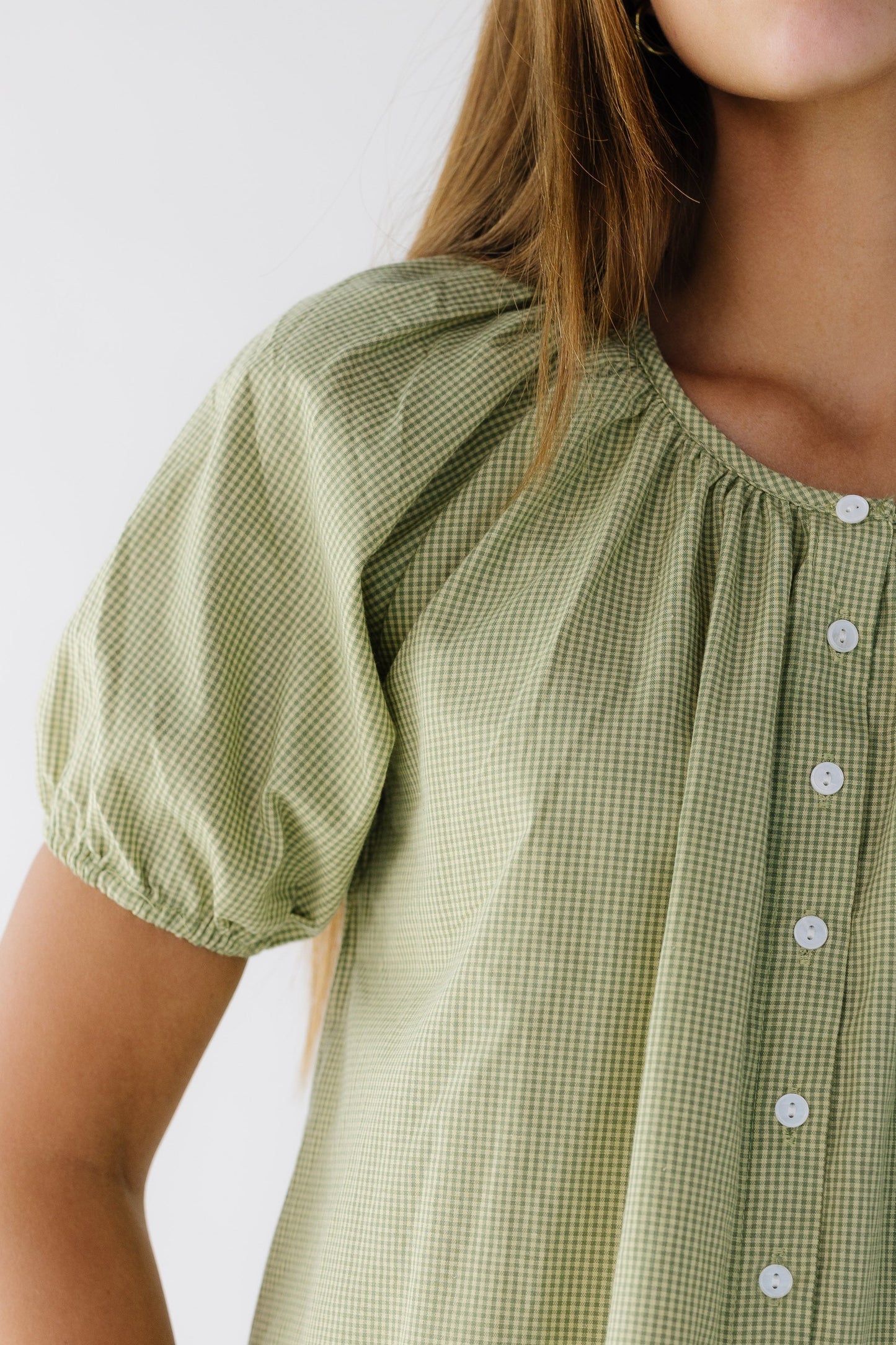 Close view of a woman wearing a green gingham blouse with a short puff sleeves.