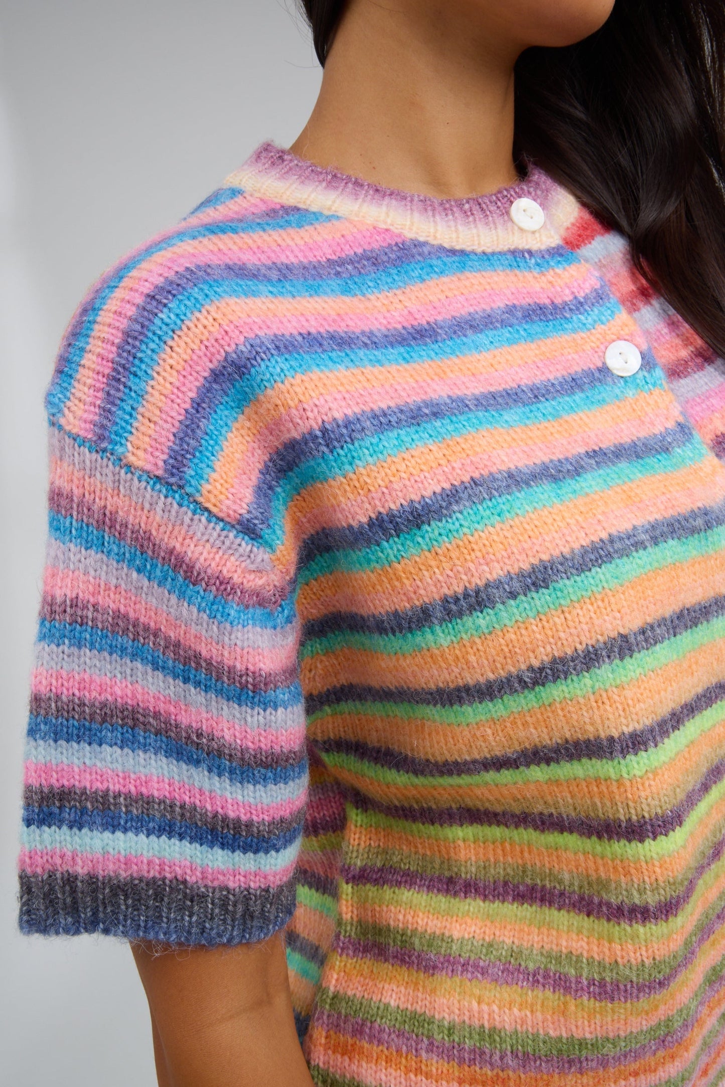Close view of a woman wearing a short sleeve rainbow stripe cardigan.