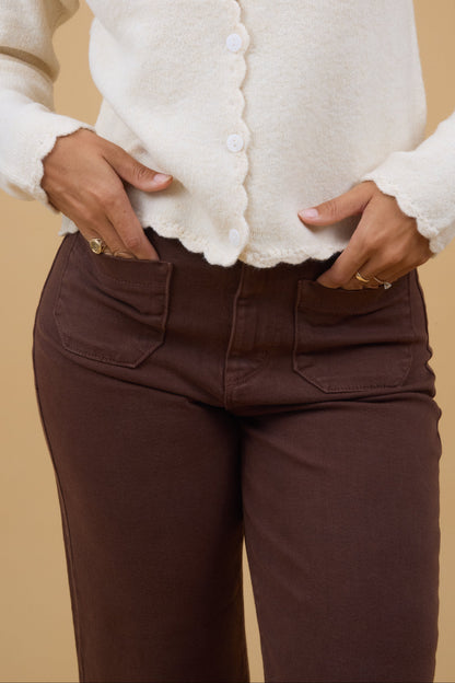 Close view of a young woman wearing a air of brown jeans with 2 front patch pockets.