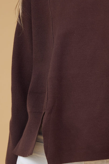 Close view of a young woman wearing a knit top in a ribbed fabric side panels, smooth ront panel and short slit at the hip.
