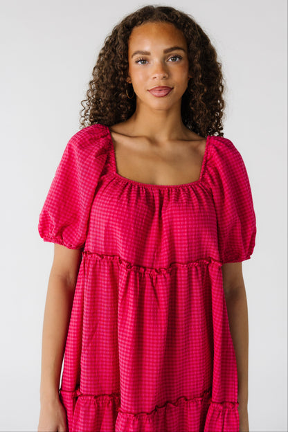 Teenage girl wearing a pink gingham, tiered dress with a square neckline and and large puff sleeves.
