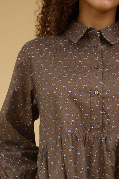 Close view of a teenage girl wearing brown print dress with a button down bodice, pointed collar and long sleeves.