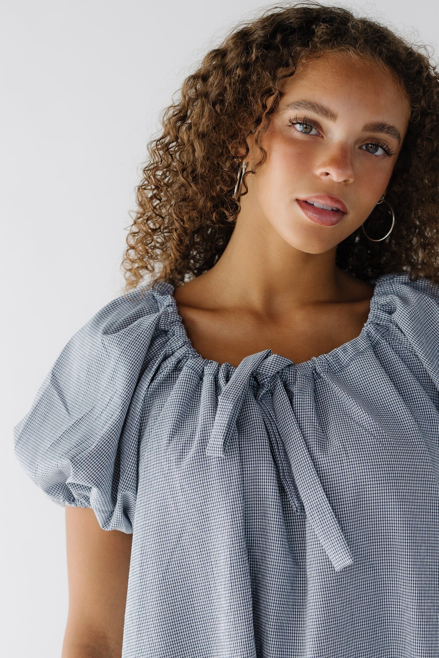 Close up view of a navy & white gingham dress with balloon sleeves and a drawstring-scoop neckline.