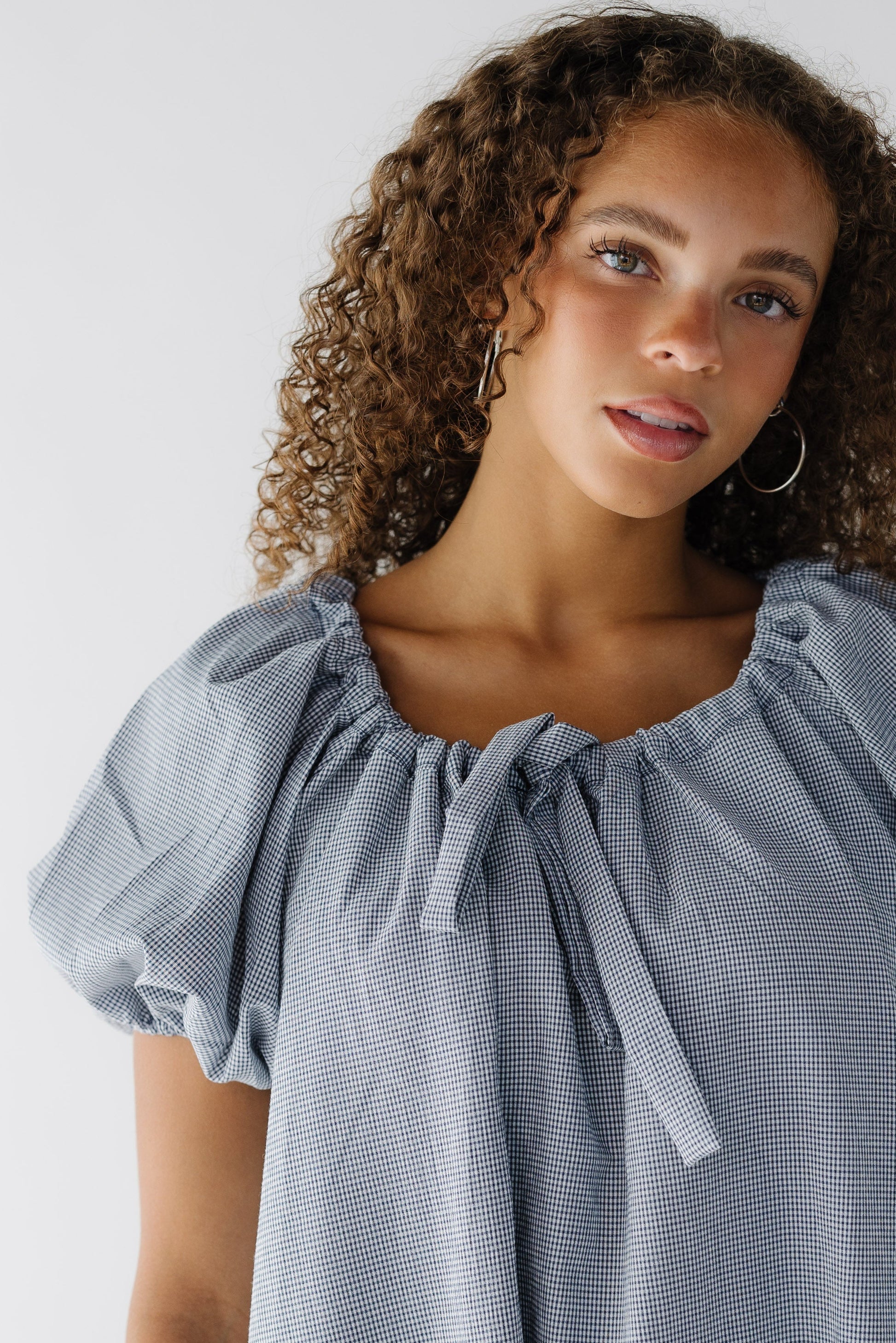 Close up view of a navy & white gingham dress with balloon sleeves and a drawstring-scoop neckline.