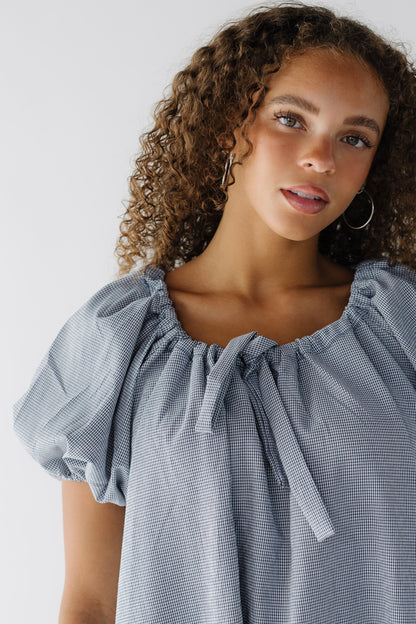 Close up view of a navy & white gingham dress with balloon sleeves and a drawstring-scoop neckline.