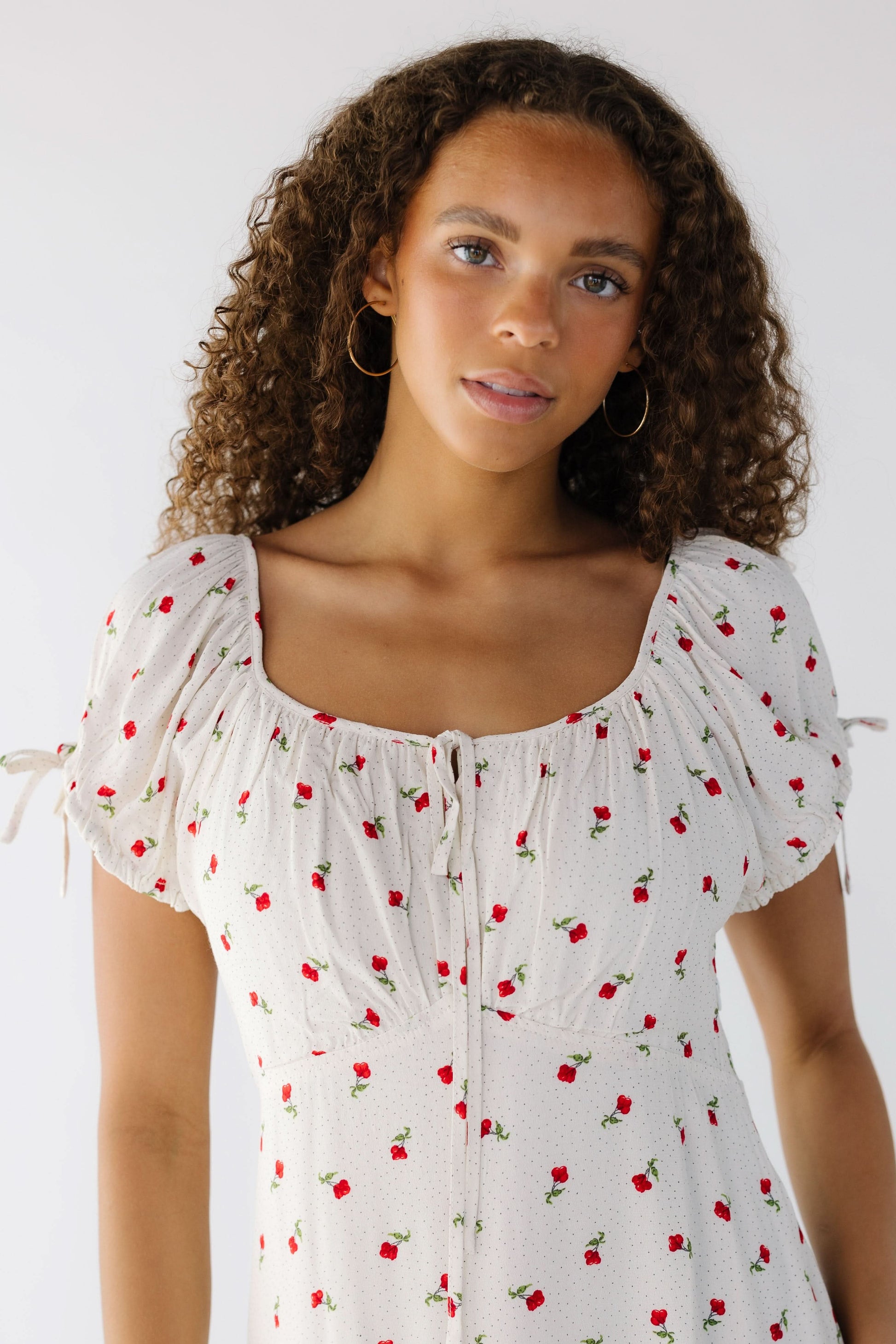 Close view of a teen girl wearing a white midi-maxi dress with red floral print, short puff sleeves and a wide scoop neckline.