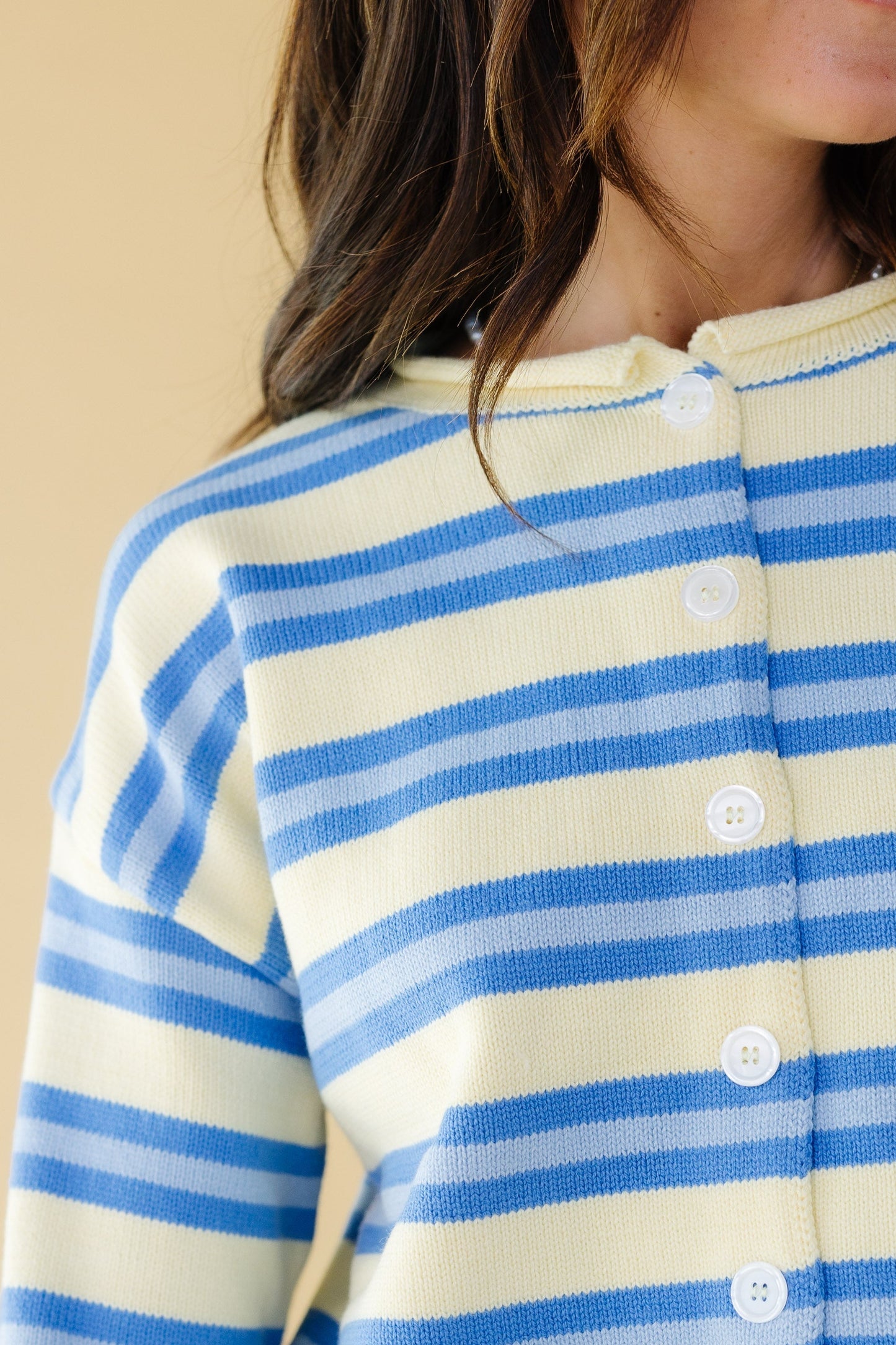 Close view of a woman wearing a yellow & blue stripe button down cardigan with long sleeves and a rolled neckline.
