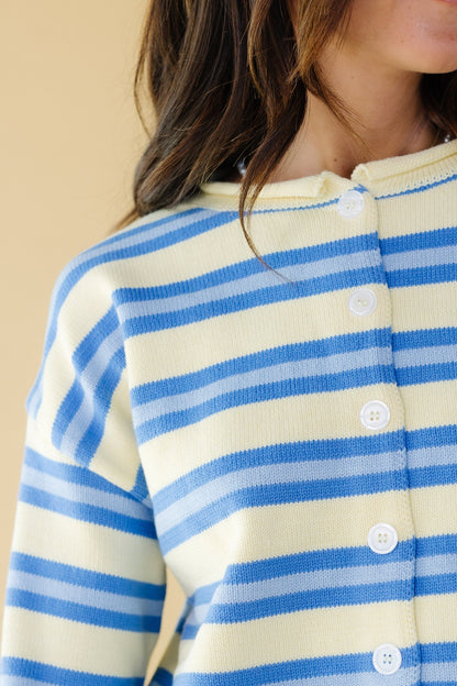Close view of a woman wearing a yellow & blue stripe button down cardigan with long sleeves and a rolled neckline.