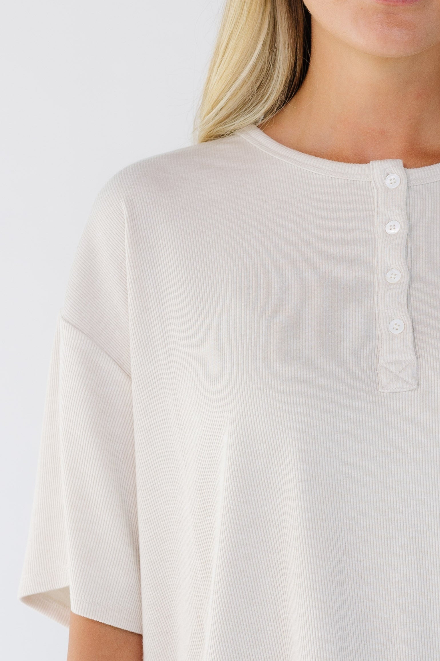 Close view of a woman wearing a beige rib knit, loose fitting top with short sleeves and a short button placket.