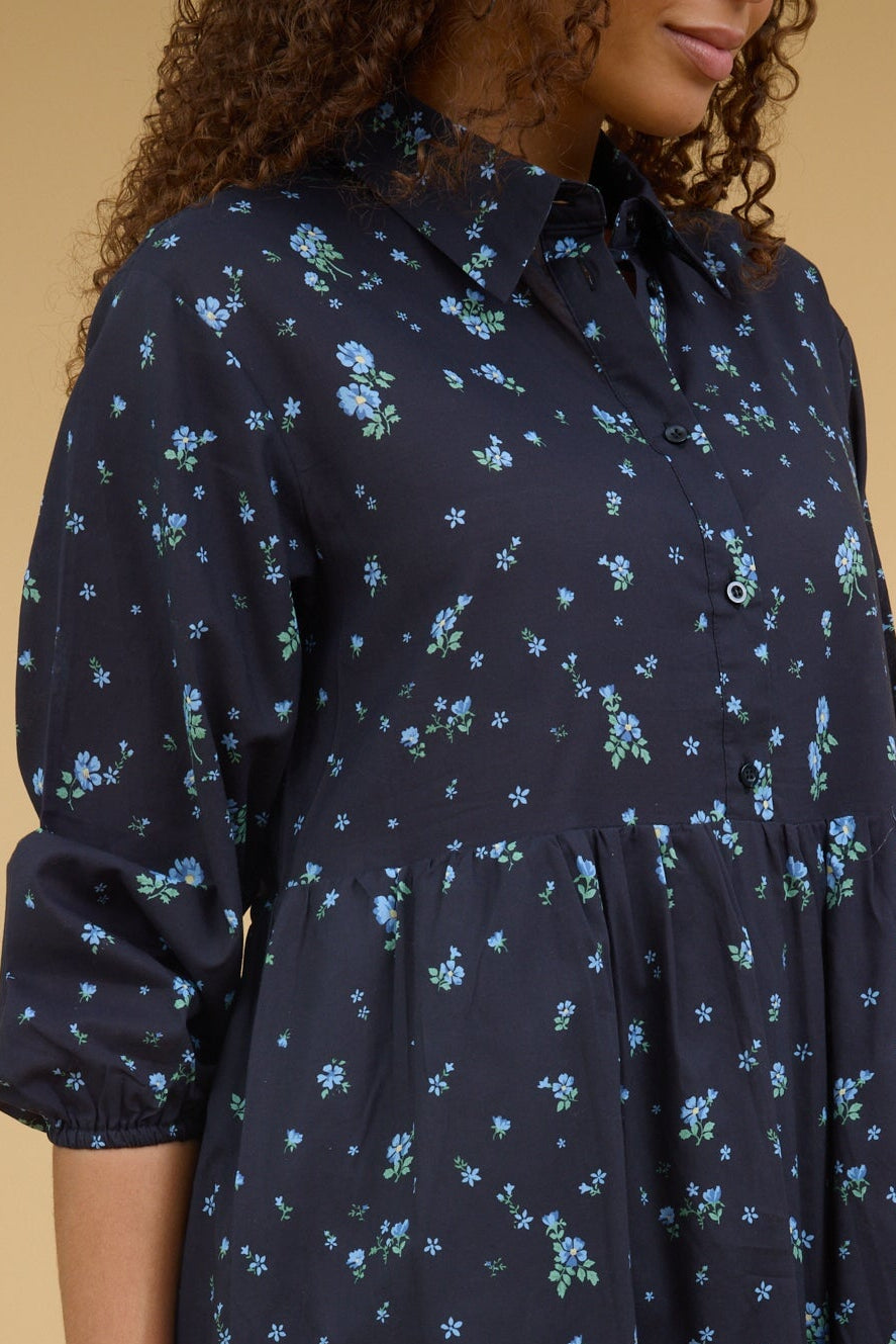 Close view of a teenage girl wearing a blue floral print dress with a button down bodice, long sleeves and a pointed collar.