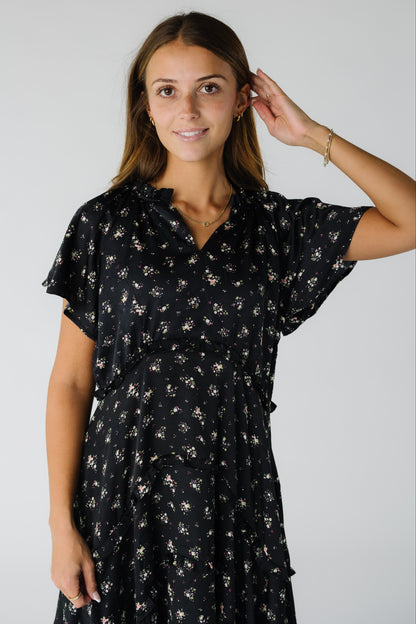 Close view of a woman wearing a black floral dress with a V-neckline and short flutter sleeves