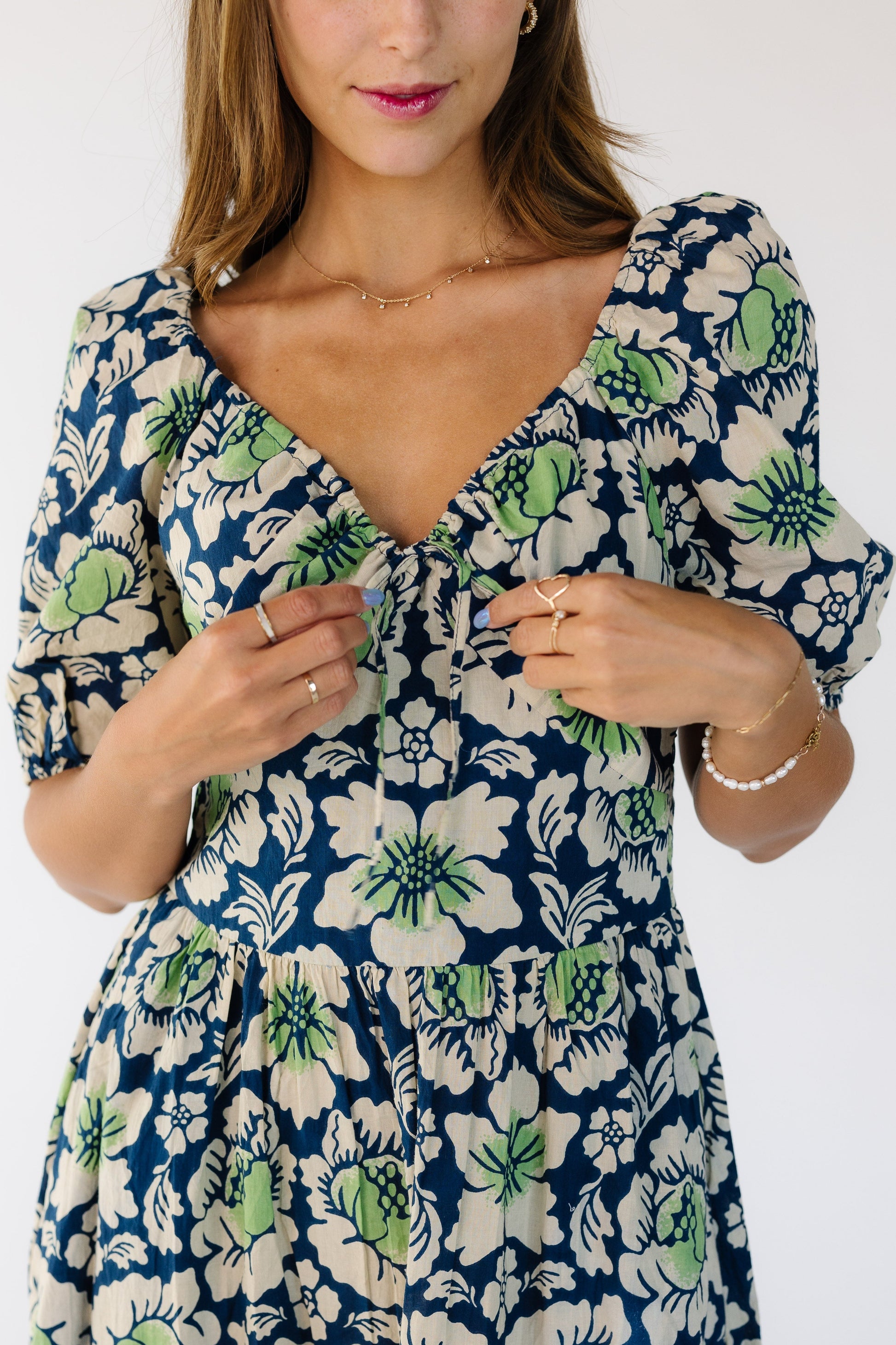 Close up view of a woman wearing a blue and green floral dress with a sweetheart neckline and an pointed empire waistband and a full skirt.