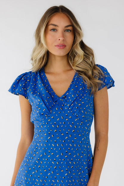 Close view of a woman wearing a blue floral print dress with a V-neckline, pointed empire waist and short flutter sleeves.