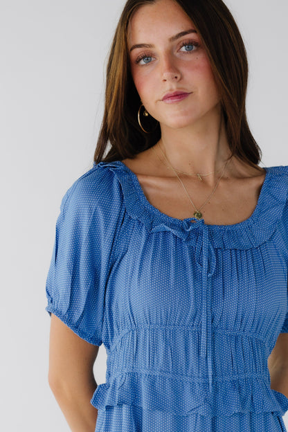 Close view of a woman wearing a blue polka dot dress with a ruffled scoop neckline, puff sleeves and a wide waist with a ruffle.