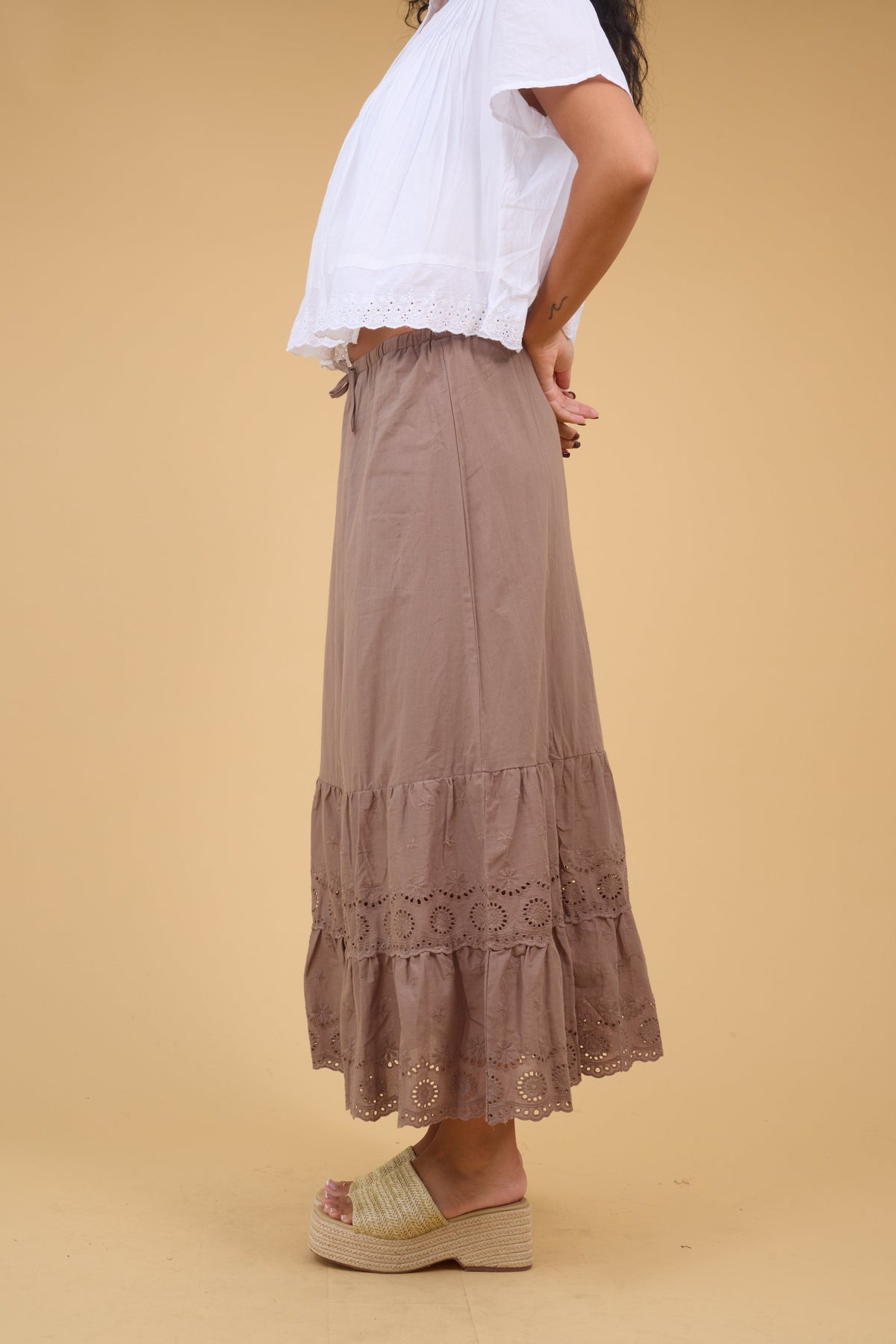 Young woman wearing a brown midi skirt with a wide eyelet ruffle.