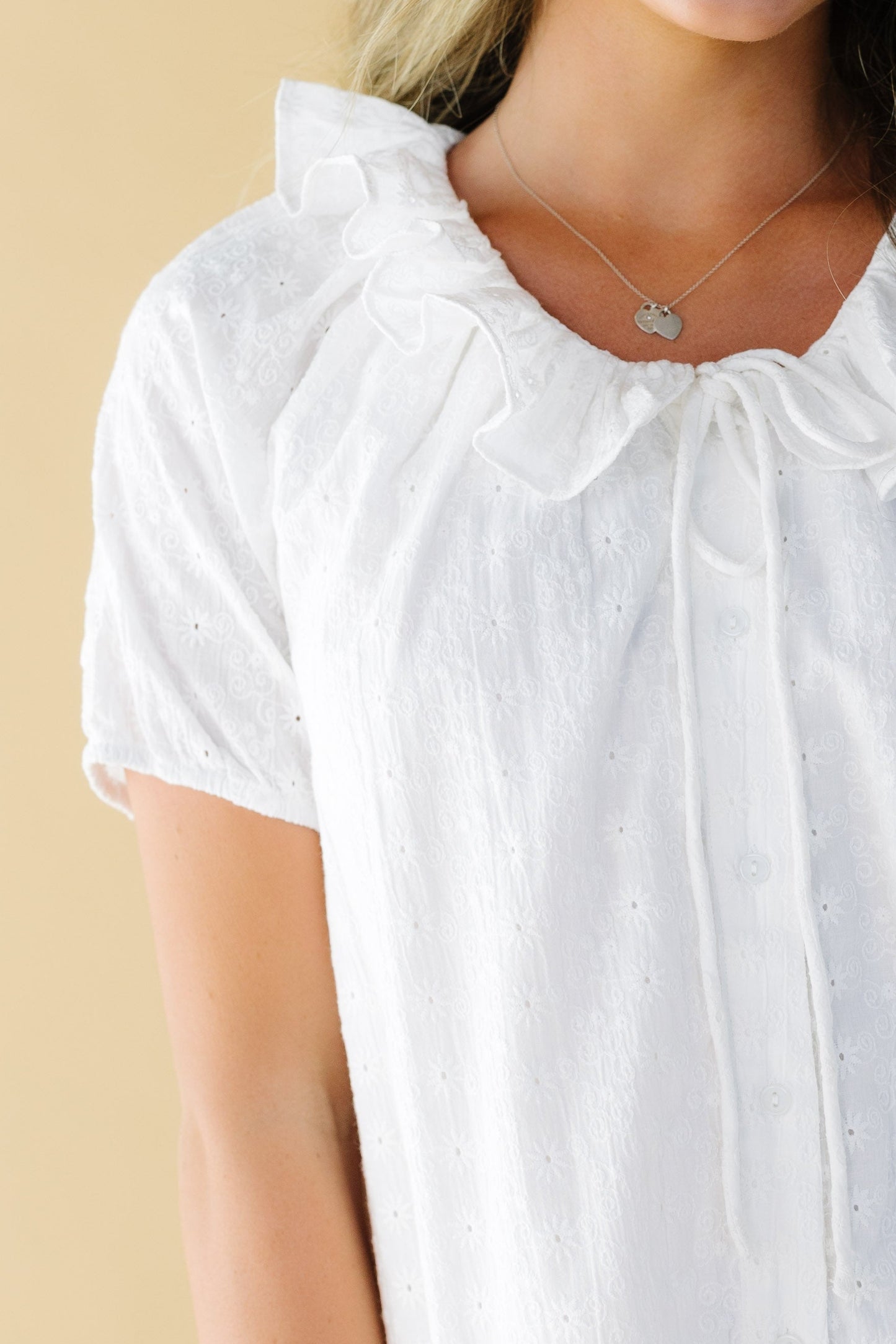 Close view of a woman wearing a white eyelet button down dress with short puff sleeves and a round ruffled collar.