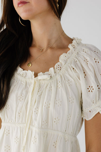 Close view of a young woman wearing a cream color eyelet blouse with a ruffle collar.