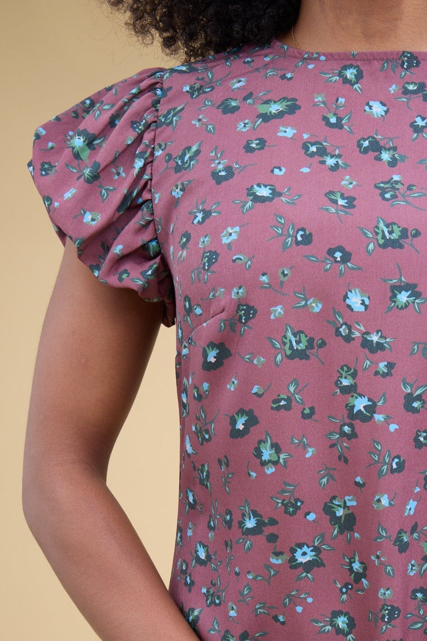 Close view of a young woman wearing a magenta floral print gathered cap sleeves and a round neckline.