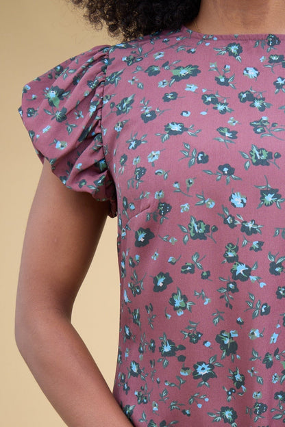 Close view of a young woman wearing a magenta floral print gathered cap sleeves and a round neckline.
