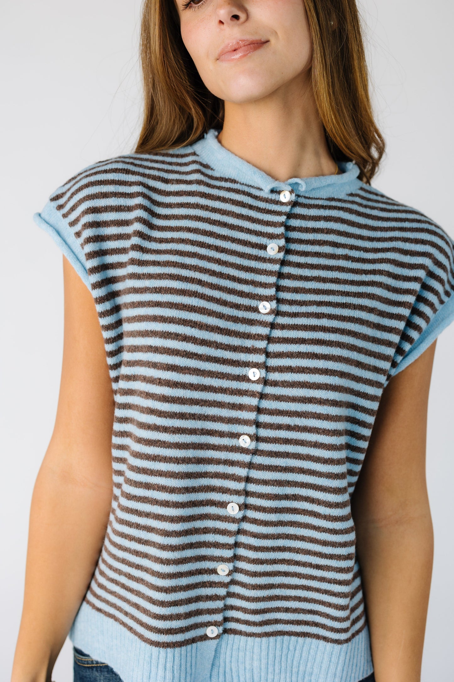 Close view of a woman wearing a light blue and brown stripe sweater vest.