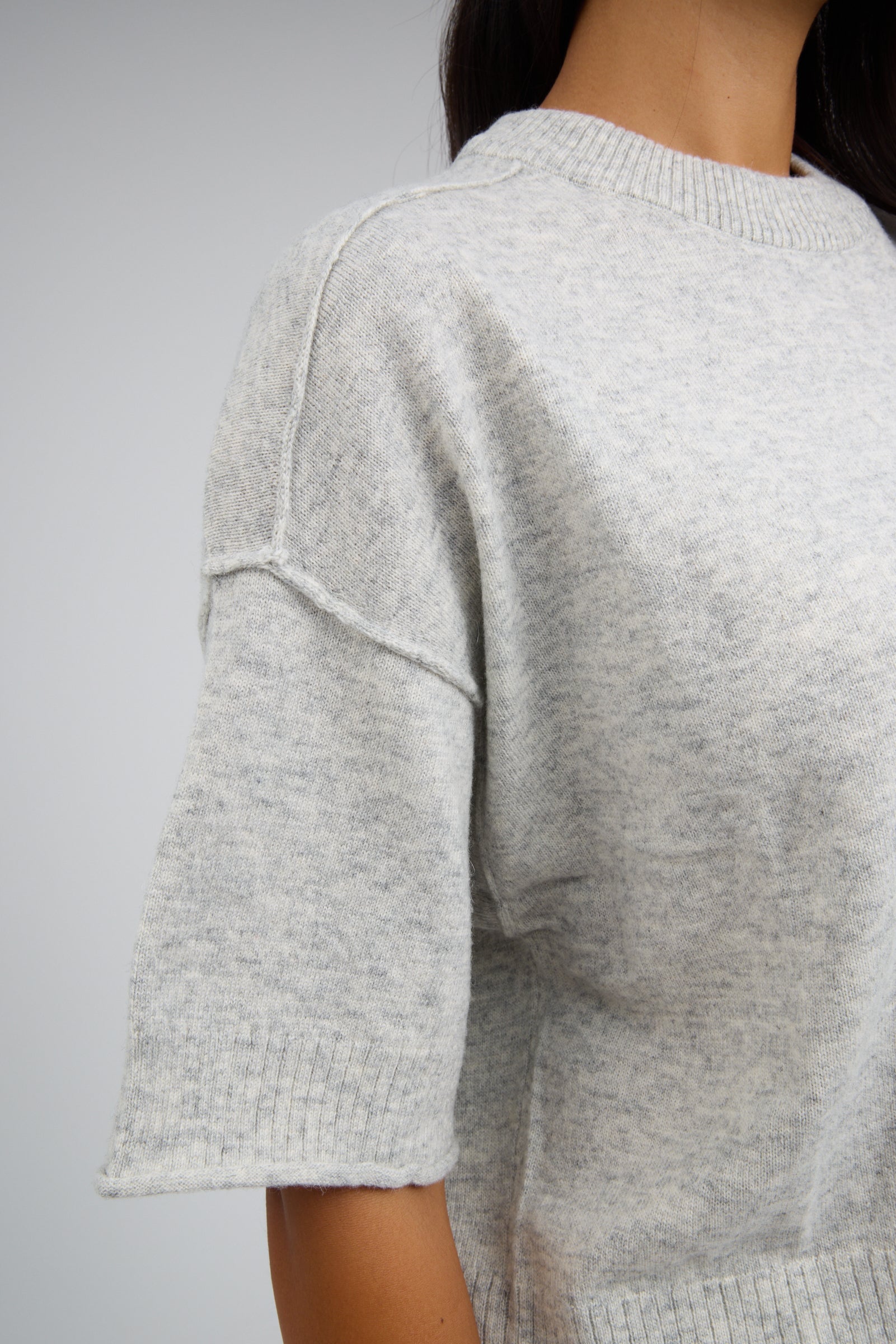 Close view of a woman wearing a lightweight heather grey sweater with elbow length sleeves and exposed sleeve details.