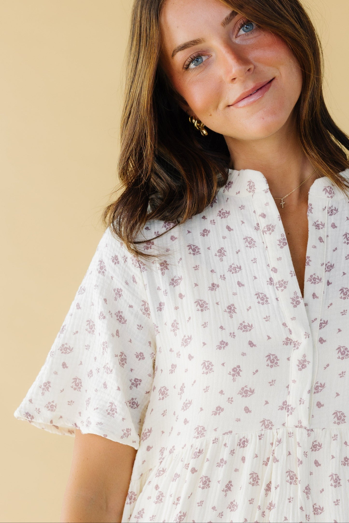 Close view of a woman wearing a cream & mauve dress with a V-neckline and short sleeves.