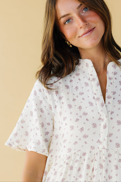 Close view of a woman wearing a cream & mauve dress with a V-neckline and short sleeves.