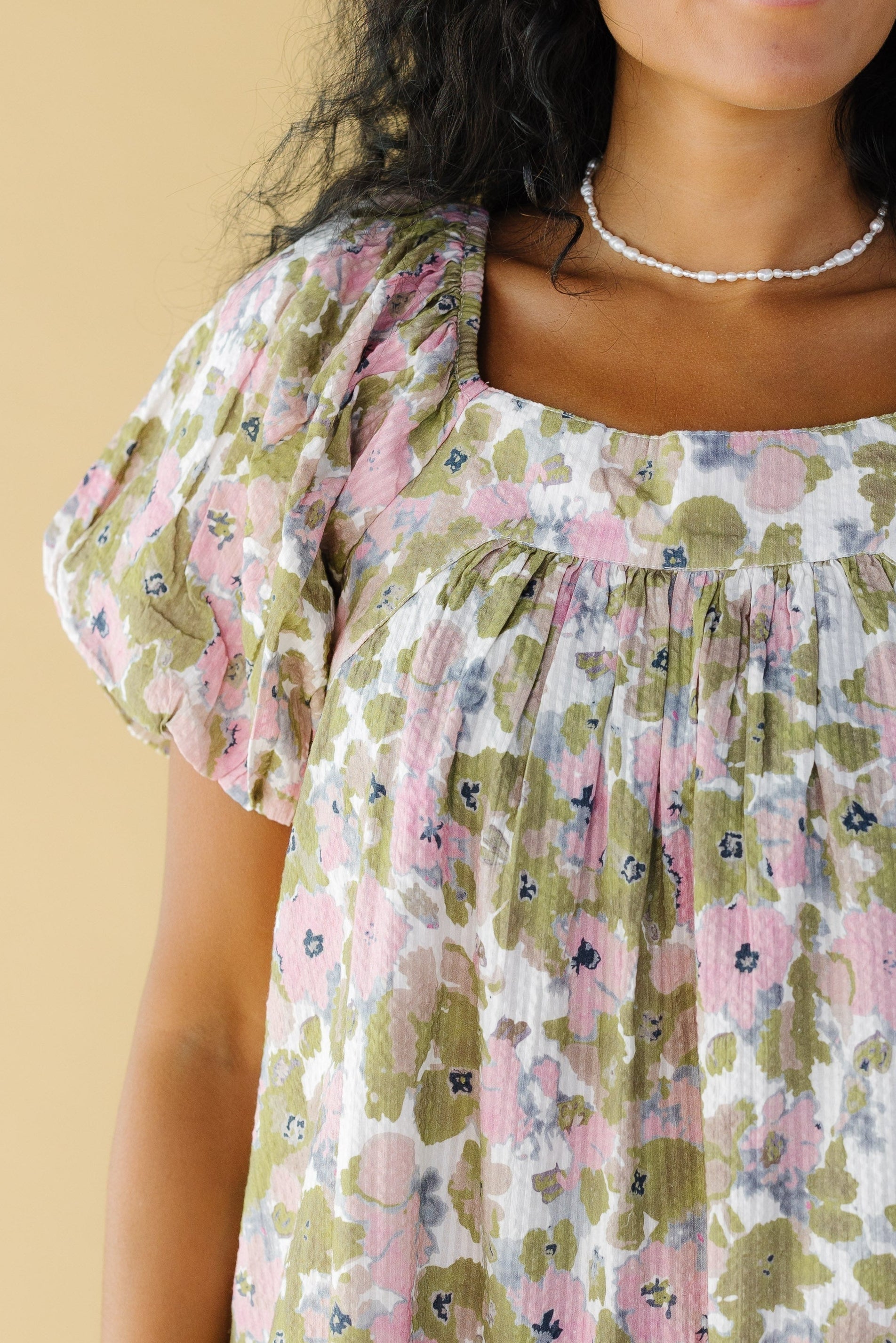 Close view of a woman wearing a pink and green floral dress with balloon sleeves and a square neckline.
