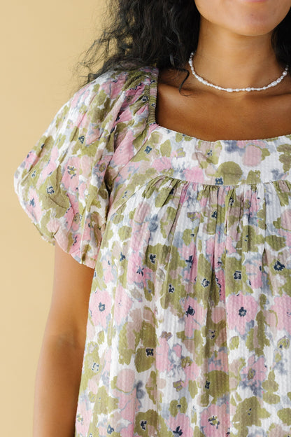 Close view of a woman wearing a pink and green floral dress with balloon sleeves and a square neckline.
