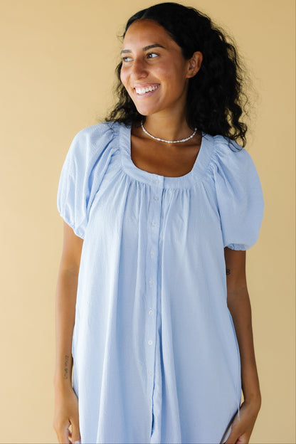 Young woman wearing a light blue line plaid button down dress with a scoop neckline and balloon sleeves.