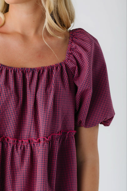 Close view of a woman wearing a red & navy gingham dress with a square elstic neckline and large puff sleeves.