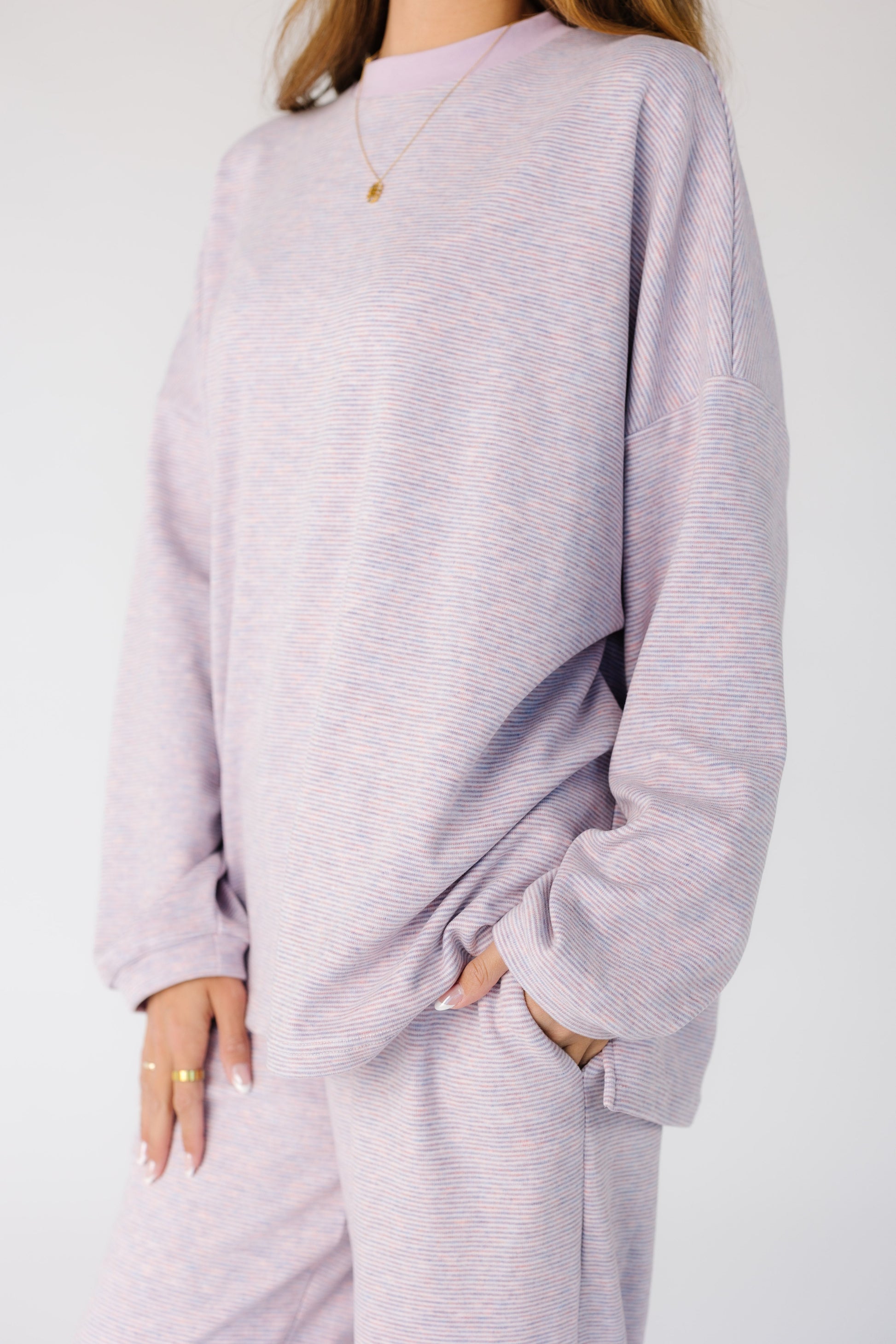 Close view of a woman wearing a pink and lavender narrow stripe lounge set with side pant pockets.