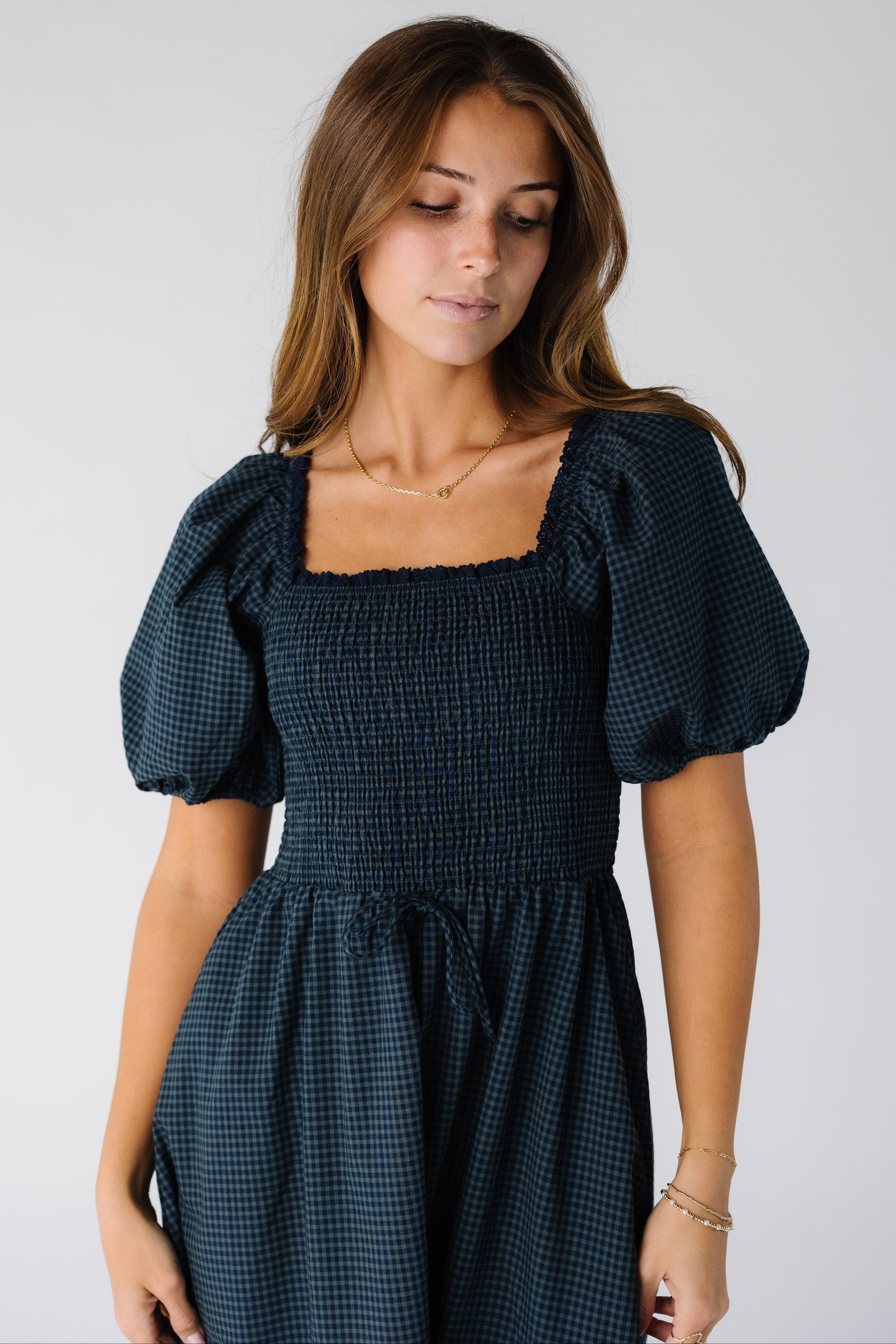 Close view of a woman wearing a navy gingham dress with a smocked bodice, square neckline and short sleeves