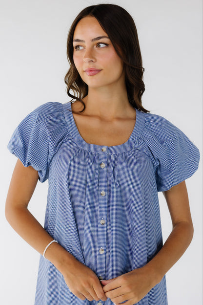 Close up view of a young woman wearing a navy & white gingham button down dress with balloon sleeves and a scoop neckline.