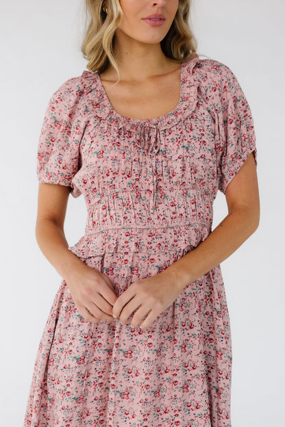 Close view of a young woman wearing a pink floral print dress with a scoop ruffled neckline and a short puff sleeves and a wide waistband.