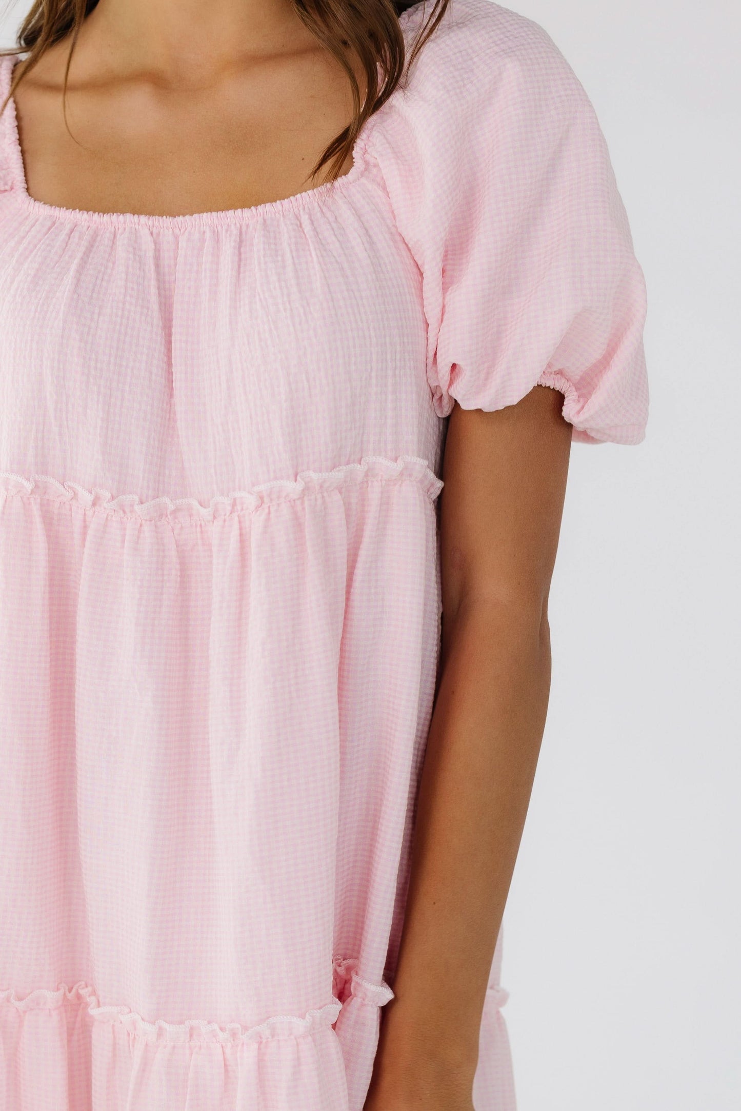 Close view of a woman wearing a pink gingham tiered midi dress with balloon sleeves and a square neckline.
