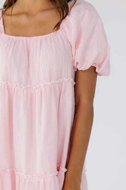 Close view of a woman wearing a pink gingham tiered midi dress with balloon sleeves and a square neckline.