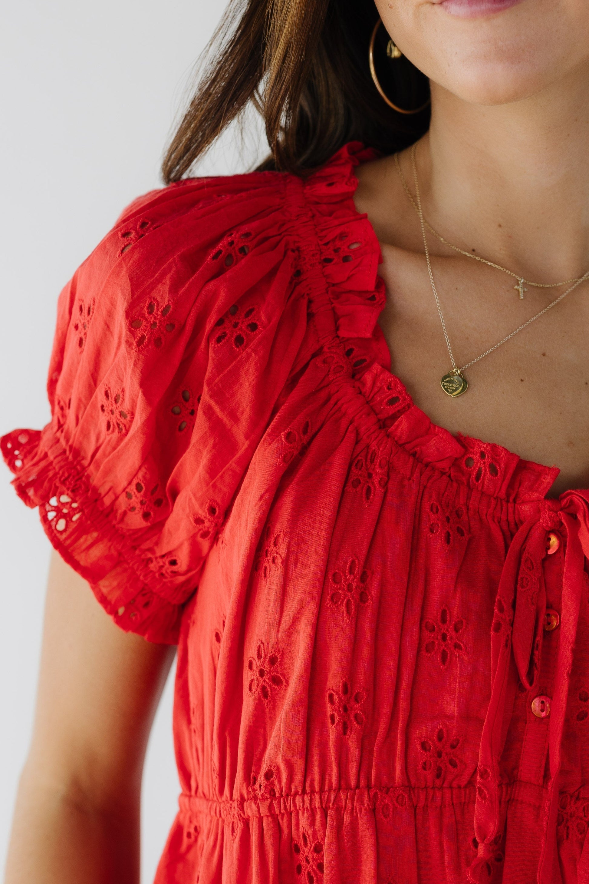 Close view of a young woman wearing a red eyelet blouse with short puff sleeves and a scoop